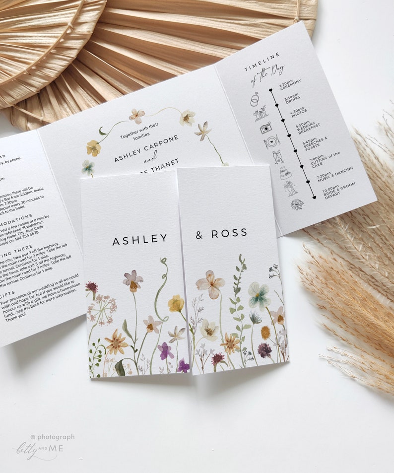 May include: A wedding invitation with a floral design. The invitation features the names Ashley Carpone and Ross Thanet, along with a timeline of the wedding day. The invitation is printed on white cardstock and has a watercolor floral design.