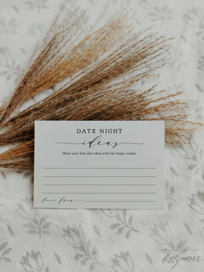 May include: A white card with the text "DATE NIGHT ideas" in elegant script. The card includes prompts to share date ideas and a space to write "love from." Dried wheat stalks and a floral patterned background complete the image.