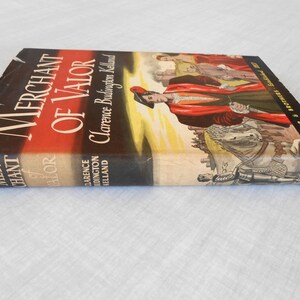 May include: A vintage hardcover book titled "Merchant of Valor" by Clarence Budington Kelland. The cover features a red and black design with an illustration of figures in period clothing. Published by Harper & Brothers.