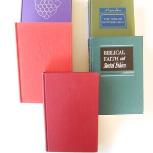 May include: A collection of five hardcover books with different colored covers. The books are stacked on top of each other. The top book has a blue spine with the title "The Foolish Gentlewoman" and the author "Margery Sharp". The second book has a green cover with the title "Biblical Faith and Social Ethics" and the author "Gardner". The third book has a red cover with a design on the front. The fourth book has a purple cover with a grape design on the front. The fifth book has a red cover with a design on the front.