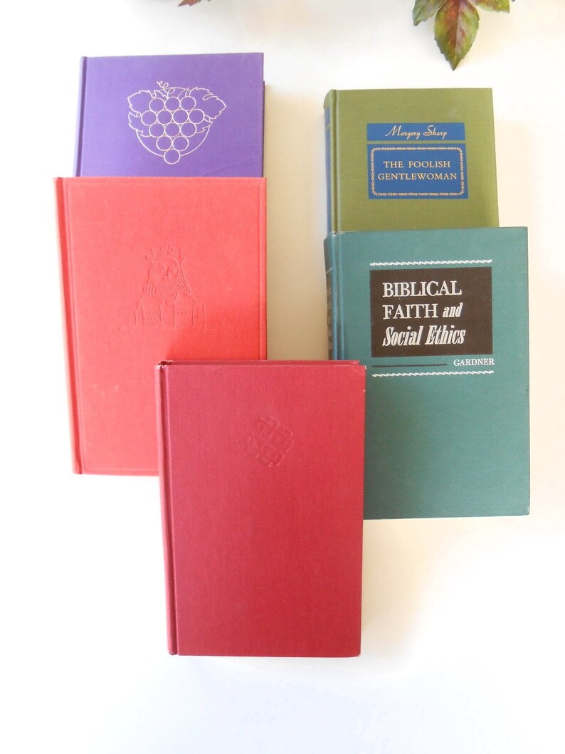 May include: A collection of five hardcover books with different colored covers. The books are stacked on top of each other. The top book has a blue spine with the title "The Foolish Gentlewoman" and the author "Margery Sharp". The second book has a green cover with the title "Biblical Faith and Social Ethics" and the author "Gardner". The third book has a red cover with a design on the front. The fourth book has a purple cover with a grape design on the front. The fifth book has a red cover with a design on the front.