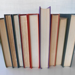 May include: A collection of ten hardcover books with different colored spines, including green, blue, beige, red, white, and purple. The books are arranged vertically in a row.