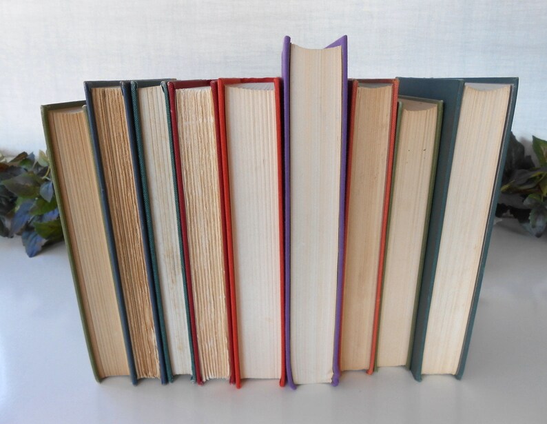 May include: A collection of ten hardcover books with different colored spines, including green, blue, beige, red, white, and purple. The books are arranged vertically in a row.
