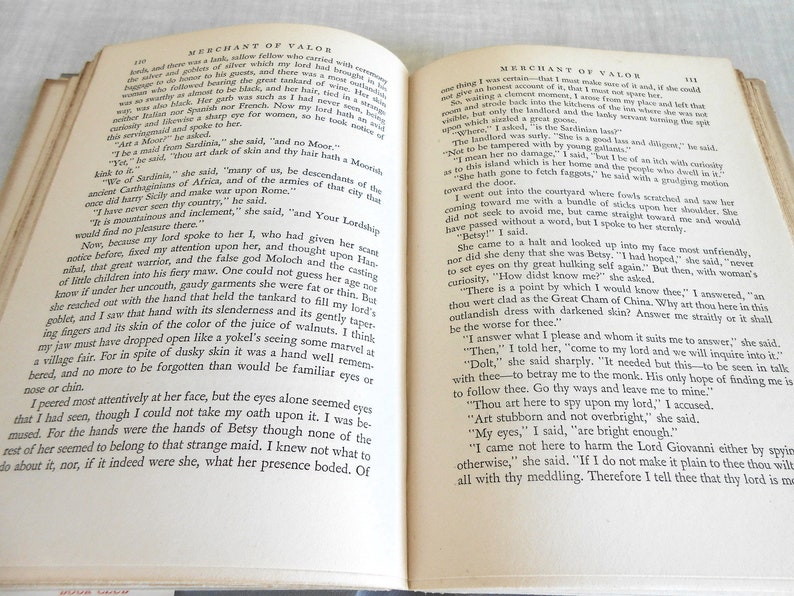 May include: Open book with aged, yellowed pages. The text is in black, with the title "Merchant of Valor" at the top. The book is open to two facing pages, with the text filling the pages.