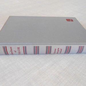 May include: A hardcover book titled "Merchant of Valor" by Clarence Budington Kelland. The book has a light gray cover and a spine with red, white, and blue striped detailing. The publisher's logo is in the upper right corner.