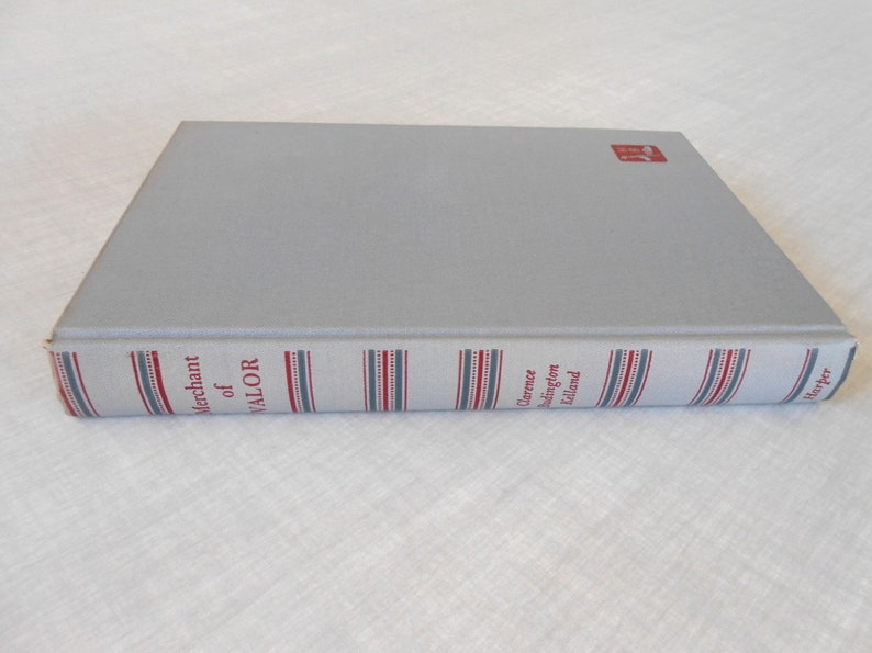 May include: A hardcover book titled "Merchant of Valor" by Clarence Budington Kelland. The book has a light gray cover and a spine with red, white, and blue striped detailing. The publisher's logo is in the upper right corner.