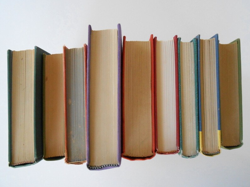 May include: A row of eight vintage hardcover books with different colored spines. The books are arranged in a row from left to right, with the spines facing the viewer. The books are all different sizes and have different titles and authors.