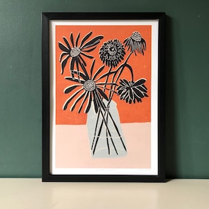 Puede incluir: Lámina artística enmarcada con una ilustración floral. Flores en blanco y negro en un jarrón transparente sobre un fondo coral y base rosa claro. El marco rectangular es negro.