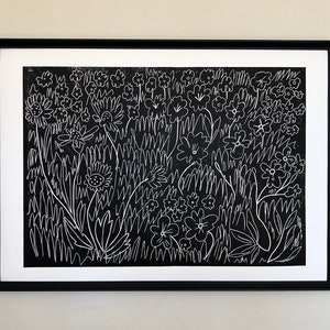 May include: A framed black and white linocut print depicting a field of flowers and grasses. The artwork uses white lines on a black background. The print is mounted within a white mount and a black frame.