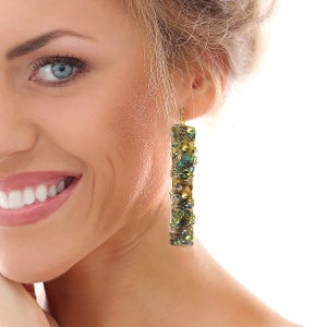 May include: Gold-toned, rectangular dangle earrings. The earrings feature a wire-wrapped design with iridescent green, blue, and gold beads and crystals. The earrings are suspended from a gold hook.