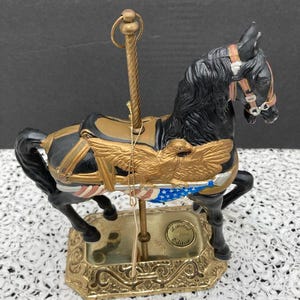 May include: A black carousel horse with gold accents and an American flag design. The horse is on a gold base with a gold pole. The base has a label that reads "Limited Edition".