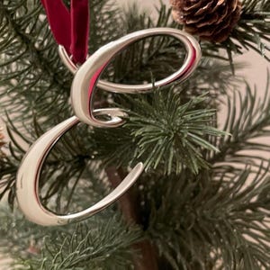 May include: A silver letter E ornament, hanging on a Christmas tree. The ornament is shiny and reflective, and the letter is in a cursive font.