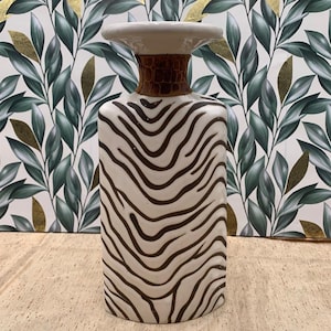 May include: A decorative ceramic vase with a zebra stripe pattern. The vase has a rectangular body, a brown textured neck, and a white top. The vase is a decorative home accent.