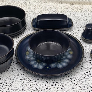 May include: A set of three ceramic mugs with a speckled, matte finish. Each mug features a different color: light blue, cream, and gray. The mugs have a simple, modern design with a rounded shape and a comfortable handle.