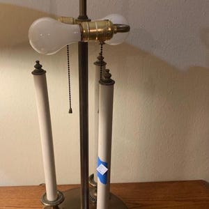 May include: An antique brass table lamp with a round base and three faux candle holders. The lamp features two light bulbs and a decorative finial. The lamp is on a wooden surface.
