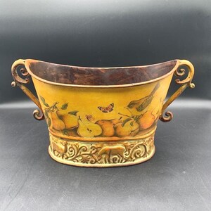 May include: Yellow metal decorative bowl with a fruit and bird design. The bowl has ornate handles and a decorative base with a relief pattern. The interior is a dark brown color.
