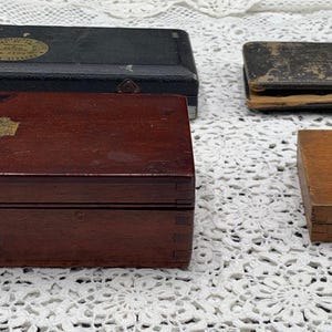 May include: Four antique wooden boxes of varying sizes and colors. The boxes range from dark green to light brown, with brass hardware and decorative metal plates. The boxes are rectangular and appear to be hinged.