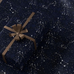 May include: Gift wrapped in dark blue paper with a constellation pattern and a brown ribbon. The paper features white constellations and stars. The ribbon is tied in a bow.