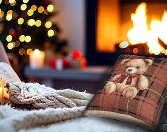 May include: A decorative pillow with a teddy bear design. The pillow features a plaid pattern in shades of brown, red, and green. The teddy bear has a red bow tie. The pillow is placed on a white blanket, with a Christmas tree and fireplace in the background.