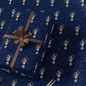 May include: A wrapped gift box with a brown ribbon and bow, placed on wrapping paper. The wrapping paper is navy blue with a repeating pattern of circus mice balancing on unicycles, with white stars scattered throughout.