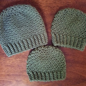 May include: Three green crocheted hats of different sizes. The hats are made with a textured stitch and have a folded brim.