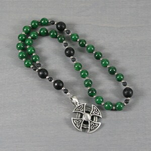 May include: A green and black beaded necklace with a silver Celtic knot pendant. The necklace is made of jade and onyx beads.