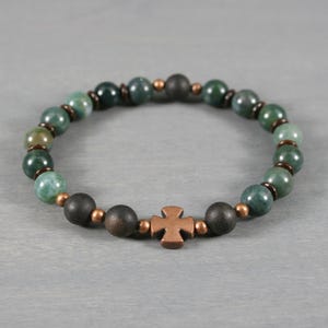 May include: A beaded bracelet featuring green and black beads with a copper cross charm. The bracelet is made with round, polished beads and small copper-colored spacers. The cross is a simple, four-armed design.
