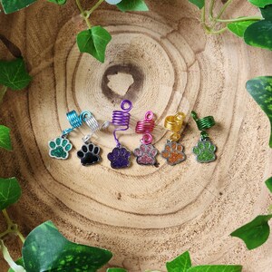 May include: Seven colourful hair coils with a paw print charm. The coils are in shades of green, purple, pink, orange, and gold. The paw prints are silver with glitter.