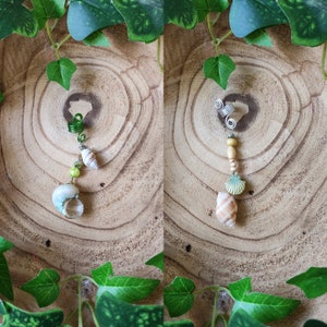 Op de afbeelding: Twee haaraccessoires met schelpbedels. De eerste accessoire is een zilveren spiraal met een groene kraal en een schelpbedel. De tweede accessoire is een zilveren spiraal met een houten kraal en een schelpbedel.