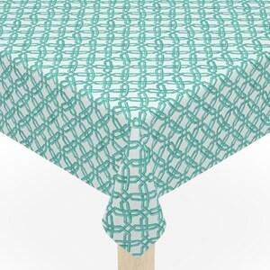 May include: A square tablecloth with a teal interlocking chain pattern on a white background. The tablecloth is draped over a square table with light-colored wooden legs.