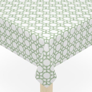 May include: A square tablecloth with a white background and a repeating green geometric pattern. The tablecloth is draped over a small wooden table with four legs.