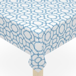 May include: A square white tablecloth with a repeating blue geometric pattern covers a small wooden table. The tablecloth has a light blue, chain-like design. The table has four light-colored wooden legs.