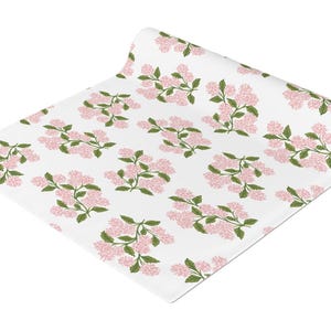 Peut inclure: Un chemin de table blanc avec un motif répété de fleurs roses et de feuilles vertes.