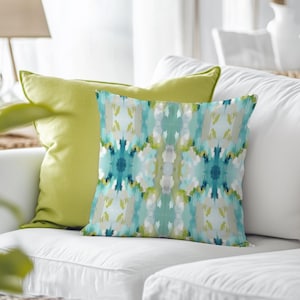 May include: A white couch with two throw pillows. The throw pillows are green and feature a blue and green abstract pattern.