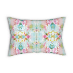 May include: A rectangular throw pillow featuring a watercolor-style abstract pattern in shades of pink, light blue, yellow, and green. The white text DREAM DECOR IDEAS is printed twice on the surface of the pillow in a serif font.