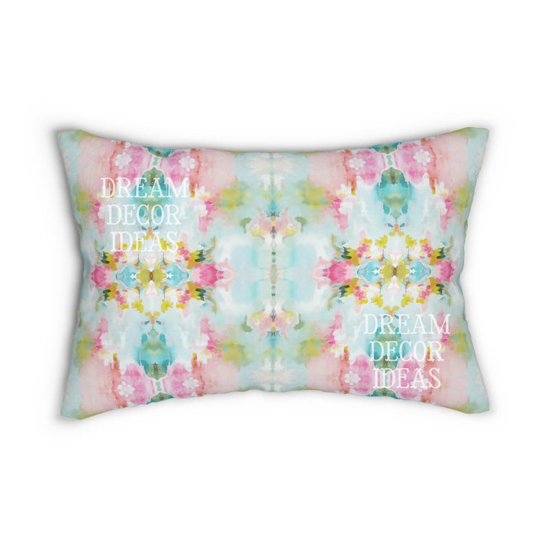 May include: A rectangular throw pillow featuring a watercolor-style abstract pattern in shades of pink, light blue, yellow, and green. The white text DREAM DECOR IDEAS is printed twice on the surface of the pillow in a serif font.
