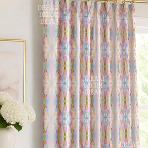 May include: A pleated curtain hanging from a gold-toned rod, featuring a vertical abstract pattern in soft shades of pink, blue, yellow, and green. The fabric displays a repeating symmetrical design with the text DREAM DECOR IDEAS overlaid.