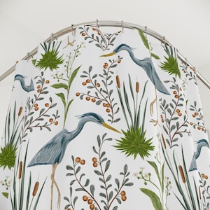 May include: White shower curtain with a repeating pattern of blue herons, green reeds, and brown berries.