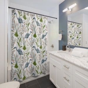 May include: A white shower curtain with a repeating pattern of blue herons, green reeds, and brown berries. The herons are standing in a marsh-like setting.
