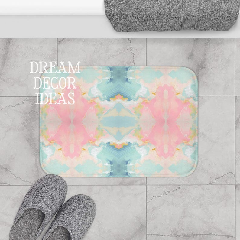 May include: A rectangular bath mat featuring a symmetrical, marbled pattern in soft shades of pastel pink, light blue, and cream. The text DREAM DECOR IDEAS is printed in white on the left side of the mat, which has rounded corners.