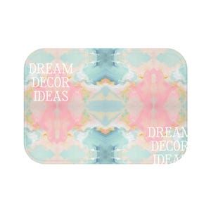 May include: A rectangular bath mat featuring a symmetrical abstract marble pattern in soft pastel shades of pink, blue, and cream. The text DREAM DECOR IDEAS is printed in white on the left side and partially repeated on the bottom right corner.