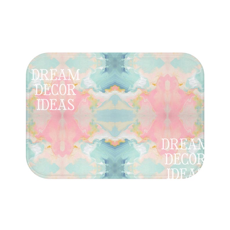 May include: A rectangular bath mat featuring a symmetrical abstract marble pattern in soft pastel shades of pink, blue, and cream. The text DREAM DECOR IDEAS is printed in white on the left side and partially repeated on the bottom right corner.