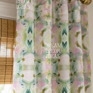 May include: A curtain panel hanging from a gold metal rod with rings, featuring a repeating watercolor-style floral pattern in shades of soft pink, sage green, and white. The text DREAM DECOR IDEAS is printed multiple times across the fabric.