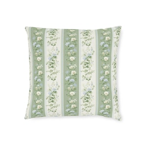 May include: Square decorative pillow with a floral pattern. The pillow features vertical stripes of green, white, and light blue. The stripes are adorned with floral arrangements in shades of white, green, and blue. The pillow is a square shape.