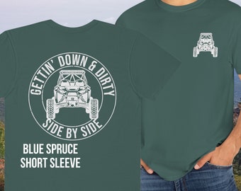Może przedstawiać: Zielony T-shirt z krótkim rękawem z białym nadrukiem terenowego pojazdu i tekstem "Gettin' Down & Dirty Side By Side" na plecach. Przód koszulki ma mały biały nadruk terenowego pojazdu. Tekst "Blue Spruce Short Sleeve" jest nadrukowany pod grafiką na plecach.