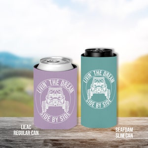 Op de afbeelding: Twee ge&iuml;soleerde drankenhouders, &eacute;&eacute;n lila en &eacute;&eacute;n zeegroen, met een witte afbeelding van een side-by-side voertuig en de tekst "Livin' the Dream Side by Side".