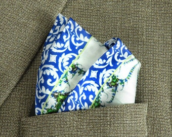May include: A blue and white patterned pocket square with green accents. The pocket square is folded and placed in the pocket of a brown blazer.