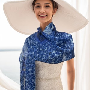Peut inclure: Une femme portant une robe blanche avec une écharpe à motifs bleus et blancs et un grand chapeau de soleil blanc.