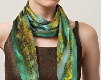 May include: A green silk scarf with a colorful geometric pattern. The scarf is tied around the neck of a person wearing a brown tank top.