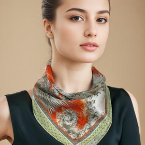 May include: A square silk scarf with a swirling orange and gray design. The scarf has a green and white dotted border. The scarf is around the neck.
